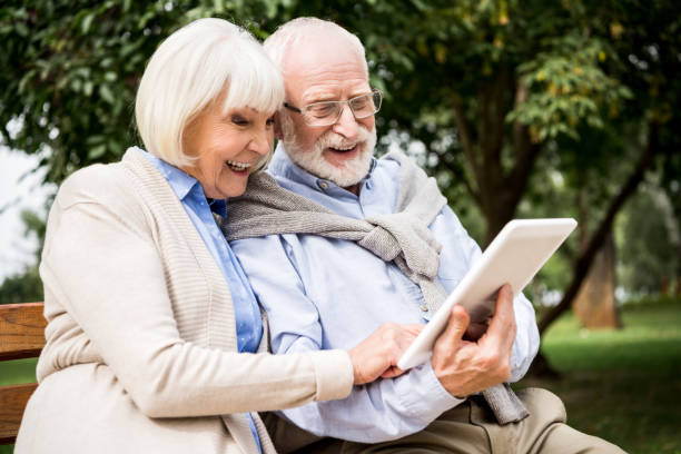 istock smiling senior couple using digital tablet while sitting on bench in park 1151874203