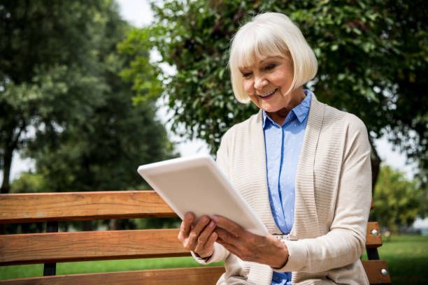 istock smiling senior woman using digital tablet while sitting on wooden bench in park 1151874208