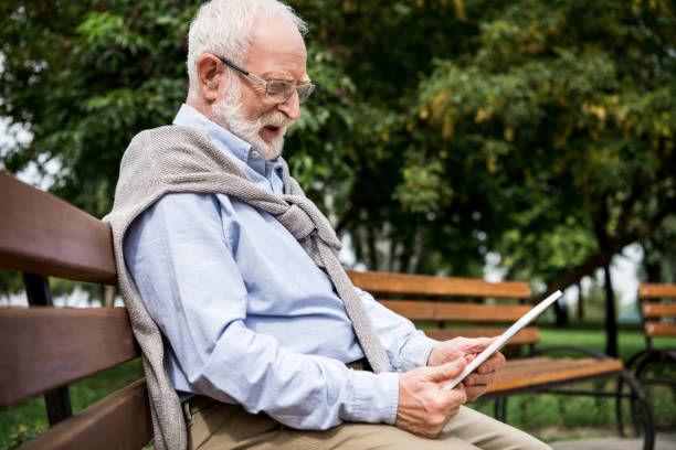 istock selective focus of senior man using digital tablet while sitting on wooden bench in park 1151874213