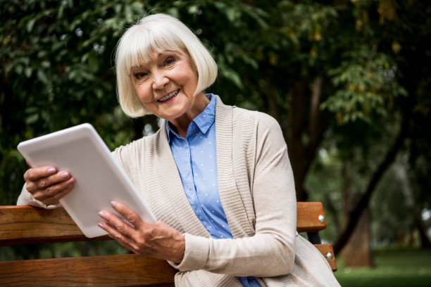 istock happy senior woman using digital tablet while sitting on wooden bench 1151874217