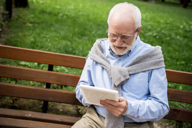 istock smiling senior man using digital tablet while sitting on wooden bench 1151874219