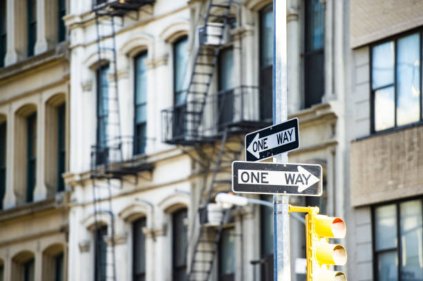 close-up view of 'one way' road sign with blurred building in the background. manhattan, new york city, united states of america. - two way traffic imagens e fotografias de stock