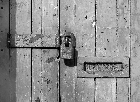 close up of an old wooden door with cracked faded paint and a rusty closed padlock and old metal letterbox