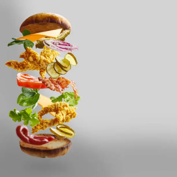 Delicious chickenburger with flying ingredients on gray background