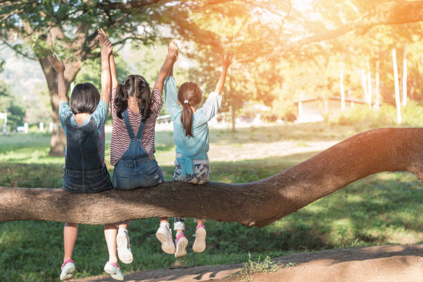 concept d’amitié d’enfants avec les gosses heureux de fille dans le parc ayant l’amusement s’asseyant sous l’arbre jouant ensemble appréciant la bonne mémoire et le moment du mode de vie d’ami d’étudiant dans le jour de l’heure d’ét� - jour des enfants photos et images de collection