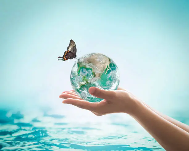 Saving water, world water day, environmental ecology protection, earth day concept with woman's hand holding green planet on blur sea or ocean background. Element of this image furnished by NASA