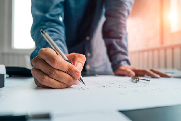 istock engineers pointing to building on blueprint and using laptop to drawing design building Project in office, construction concept. Engineer concept 1151895307