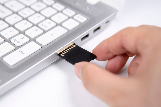 istock Human hand plugging in an SD media card into the personal laptop computer on white background. 1151903157