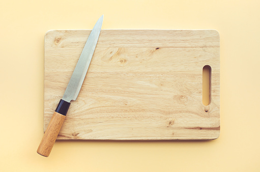 Knife on wooden chopping board on pastel color background