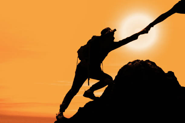 istock silhouette of man climbing up mountain with hand giving help 1151908982