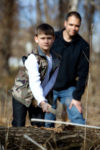 young boy and father outdoors chopping wood in the forest