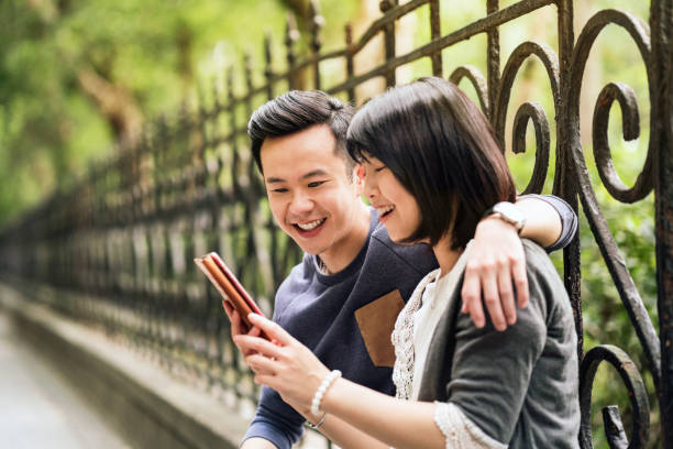 istock Happy couple looking at mobile phone against fence 1151925662