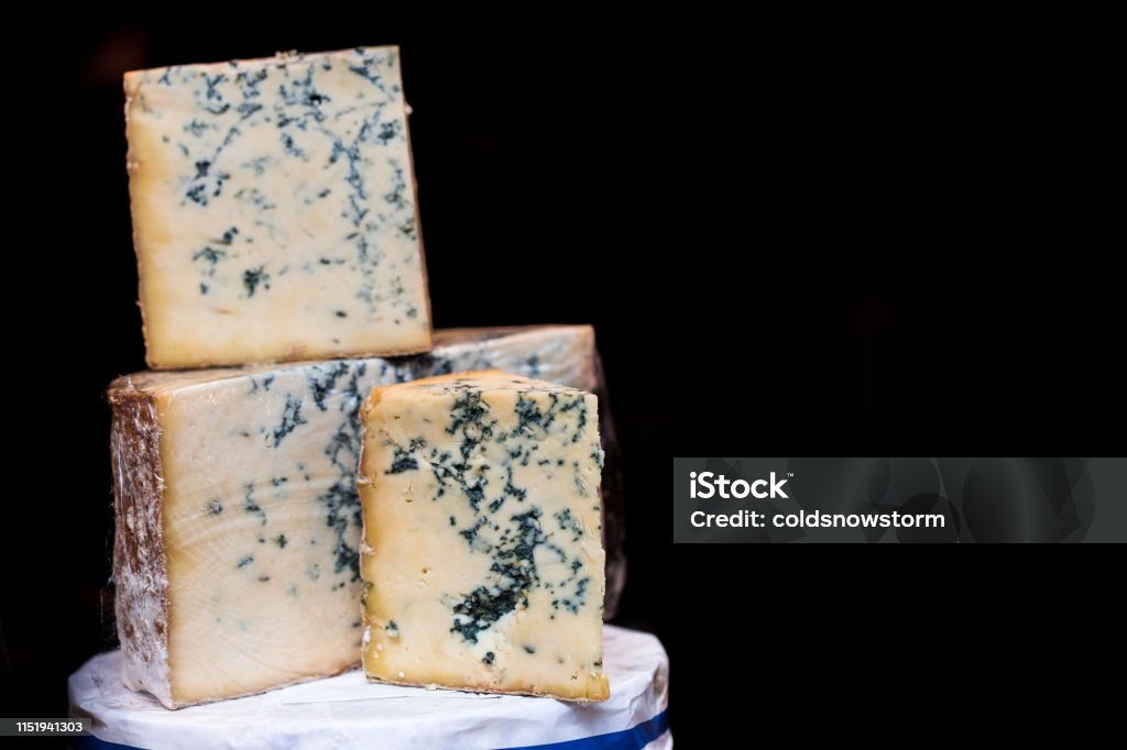 Fresh British Stilton cheese for sale at Food Market Horizontal color image depicting fresh British stilton cheese (a blue cheese) on display and for sale at Borough Market, London, UK. Focus is on three wedges of cheese in the foreground, while the background is entirely black. Room for copy space. Stilton Cheese Stock Photo