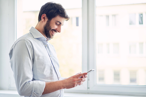 Young man using smartphone and laughing at office