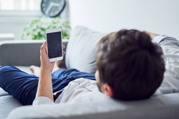 istock Young man lying on sofa and looking at phone 1151947252