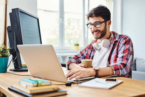 młody projektant stron internetowych pracuje nad kodem i pije kawę w swoim domowym biurze - computer programmer laptop men nerd zdjęcia i obrazy z banku zdjęć