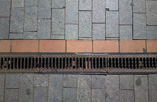 Grating of drainage system rainwater in the park at the sidewalk from a stone shaped paving slabs. top view