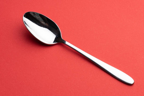 A teaspoon of shiny stainless lies on the table on a pink background.