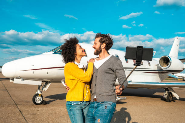 istock Rich young couple looking at each other while taking a selfie on a mobile phone on a selfie stick in front of a private jet parked on an airport tarmac 1151955365