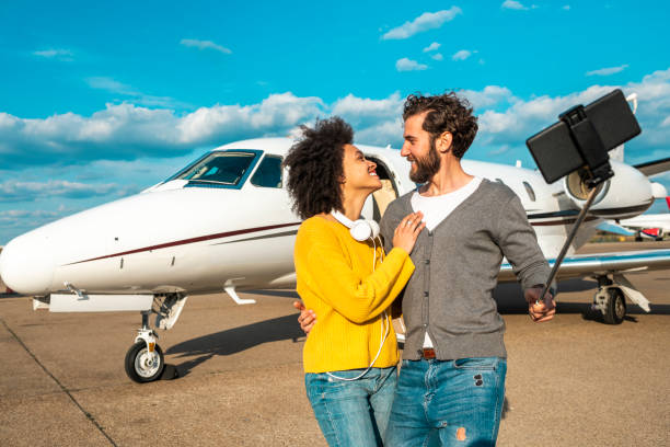 istock Rich young couple looking at each other while taking a selfie on a mobile phone in front of a private jet parked on an airport tarmac 1151955614