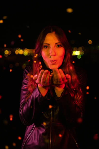 istock Young woman blowing confetti at night party 1151955828