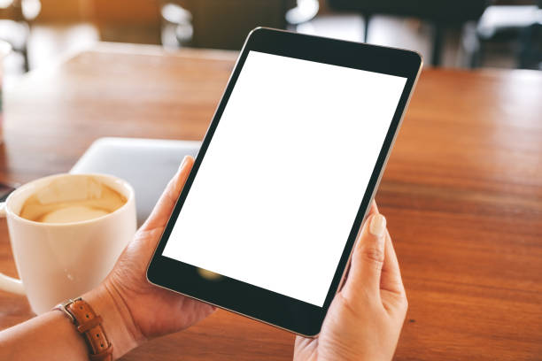 istock Mockup image of hands holding black tablet pc with blank white screen with coffee cup on wooden table 1151958720