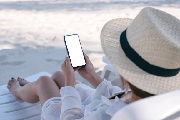 istock A woman holding white mobile phone with blank desktop screen while laying down on beach chair on the beach 1151958739