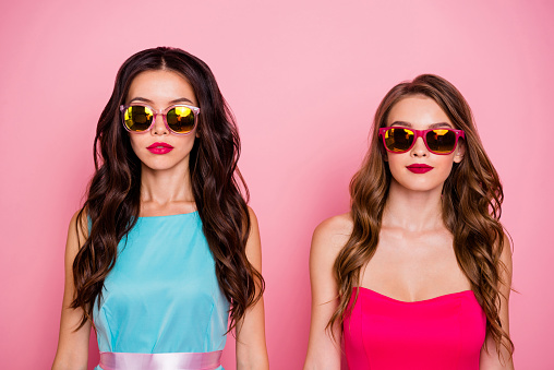 Close up photo two beautiful amazing she her ladies perfect look foreign travelers tourism classy self-confident wear sun specs shiny colorful dresses formal-wear isolated pink rose vivid background.
