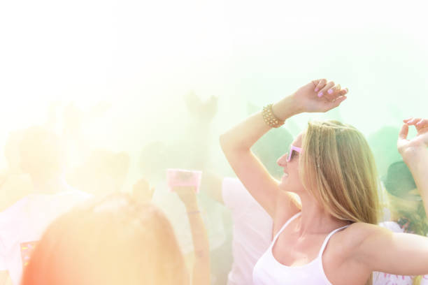 Woman loving the color festival and dancing in the crowd.  Young candid girl wearing pink sunglasses and enjoying the event.
