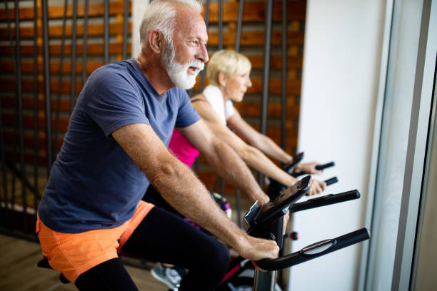 dojrzałe dopasowanie ludzi na rowerze w siłowni, ćwiczenia nogi robi cardio treningu rowerowych rowerów - spinning gym cycle cycling zdjęcia i obrazy z banku zdjęć