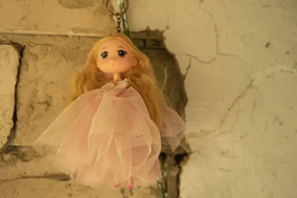 A beautiful antique doll hangs on a ruined wall of an abandoned house. Concept - mysticism, horrors.