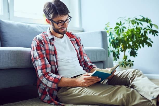 istock Happy young man reading book while sitting floor in his home 1151964047