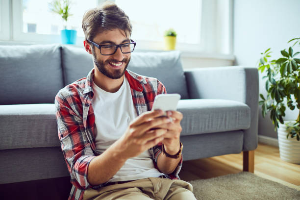 istock Smiling young man sitting on floor and texting friend 1151964575