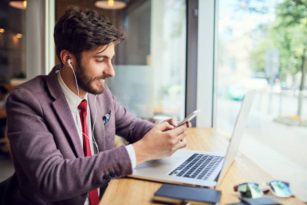 istock Always staying in touch. Side view of young handsome man texting pn phone while working on laptop in a cafe 1151967046