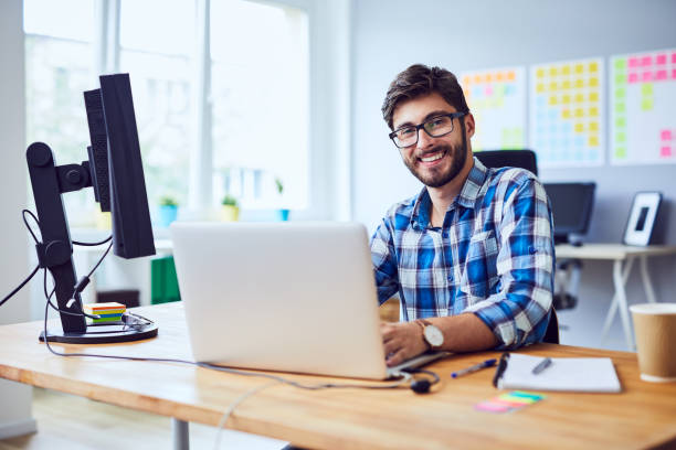 wesoły młody programista patrzący na kamerę podczas pracy w swoim biurze - computer programmer laptop nerd men zdjęcia i obrazy z banku zdjęć