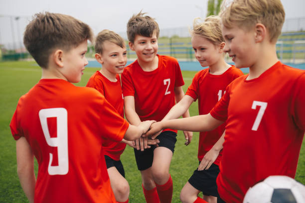 Happy boys in youth football soccer team Happy boys play team sport. Kids smiling in school sports team. Junior sports teamwork; kids put hands together. Cheerful children boys players of school soccer team. Happy boys in youth football team junior level stock pictures, royalty-free photos & images