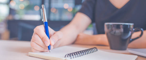 istock Woman hand is writing on a notepad with a pen in office. 1151971112