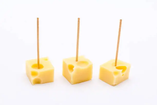Three cube shape small pieces of yellow cheese with toothpicks on white background