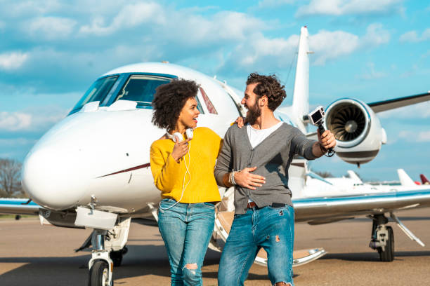 istock Famous vlogger couple making a show together with a small compact digital camera mounted on a tripod next to the nose cone of a private airplane parked on an airport taxiway 1151974747