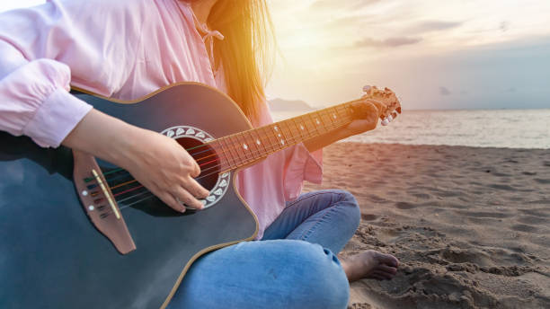 istock woman's hands playing acoustic guitar, capture chords by finger on sandy beach at sunset time. playing music concept 1151977094