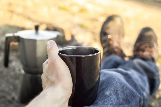 istock Preparing coffee with bonfire, resting during a camp in nature.First person view: bonfire, hiking boots, coffee maker and cup with hot coffee. 1151978548