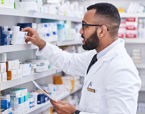 Shot of a young pharmacist working on a digital tablet while checking stock in a chemist