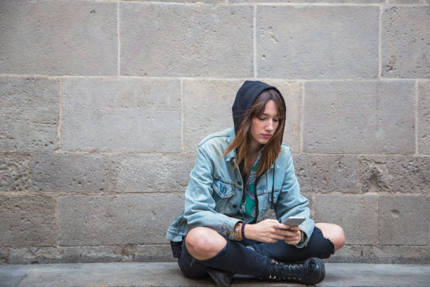 istock Young woman sitting on stone wall looking at her mobile phone 1151987351
