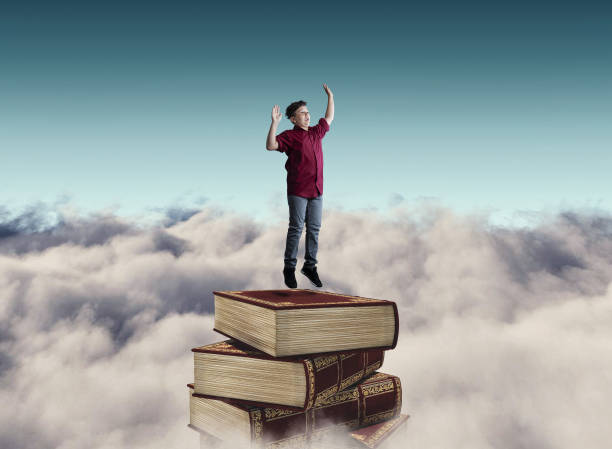 istock Young man jumping on a stack of books above clouds 1151987574
