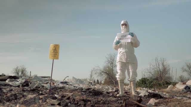 environmental movement, girl in mask and costume holding poster with stop pollution slogan at trash dump with sign biological hazard
