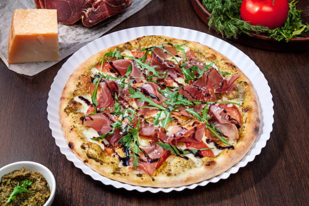 istock Top view on pizza with tomato, parmesan and prosciutto with white sauce with ingridients on brown wooden table. Picture for recipe or menu. Copy space for design. Served and cooked pizza. Italian cuisine 1151991944