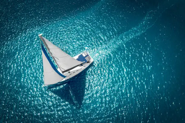 Photo of Regatta sailing ship yachts with white sails at opened sea. Aerial view of sailboat in windy condition
