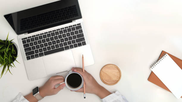 istock Female hands holding cup of coffee while working on office workspace 1151996725
