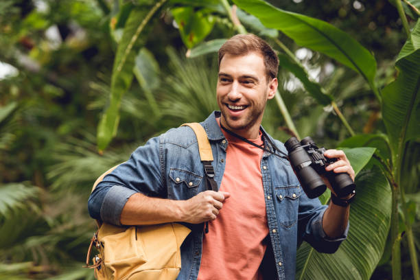 istock handsome smiling traveler with binoculars and backpack in green tropical forest 1152002422