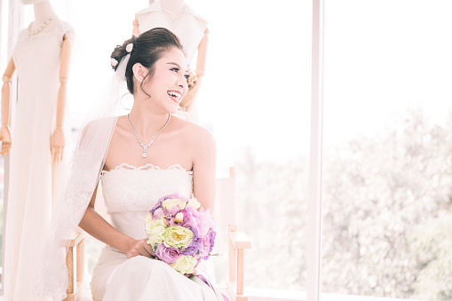 Asian Woman Bride smile in White Wedding dress with Bouquet flower in her hand with White light background